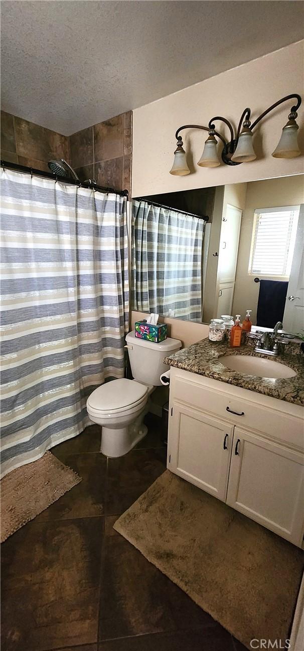 full bathroom featuring curtained shower, vanity, a textured ceiling, and toilet