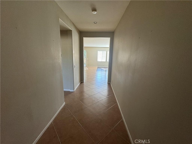 corridor featuring dark tile patterned flooring and baseboards