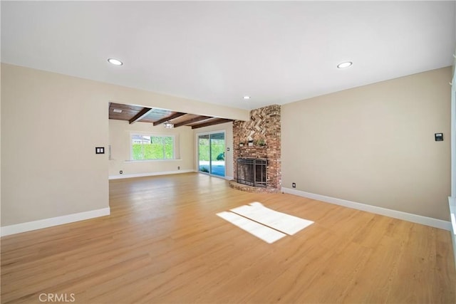 unfurnished living room with baseboards, beamed ceiling, a brick fireplace, and light wood-type flooring