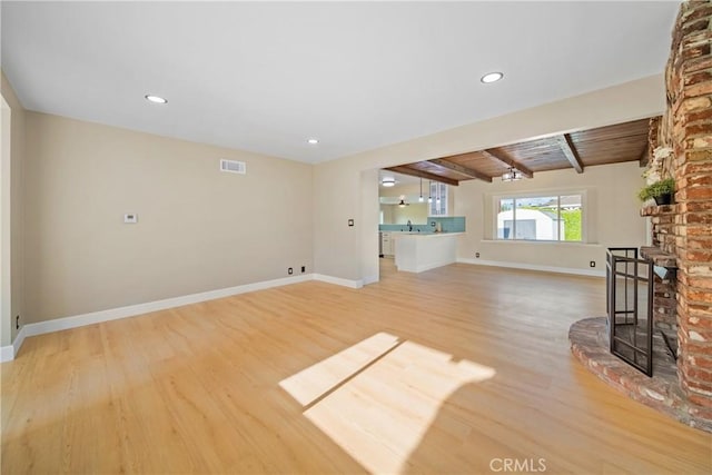 unfurnished living room with beam ceiling, a brick fireplace, baseboards, light wood-type flooring, and visible vents