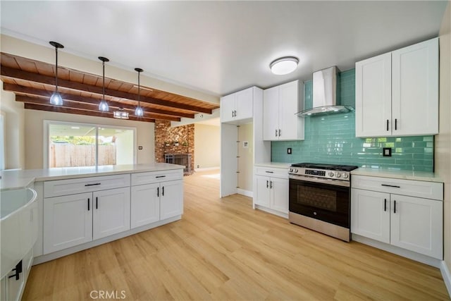 kitchen with stainless steel range with gas stovetop, a fireplace, wall chimney exhaust hood, light countertops, and light wood-style flooring