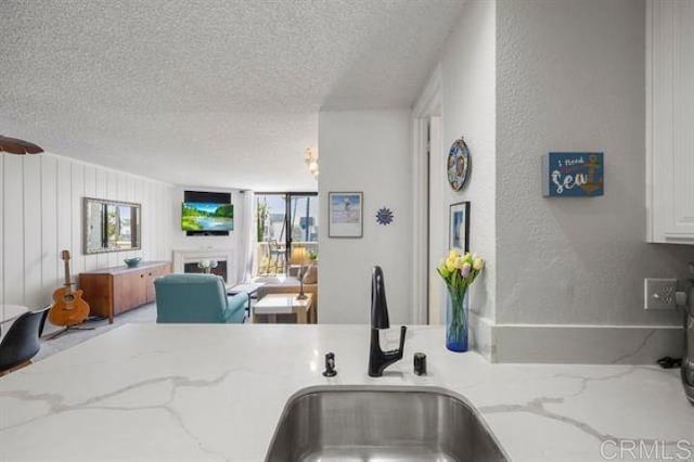 999 N Pacific St Unit G326, Oceanside, CA 92054 - kitchen with a textured ceiling, a sink, open floor plan, a textured wall, and light stone countertops