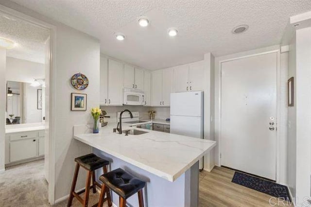 999 N Pacific St Unit G326, Oceanside, CA 92054 - kitchen with white appliances, a textured ceiling, white cabinetry, a peninsula, and a breakfast bar