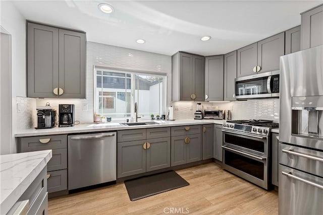 kitchen featuring light wood-style floors, tasteful backsplash, a sink, stainless steel appliances, and gray cabinetry