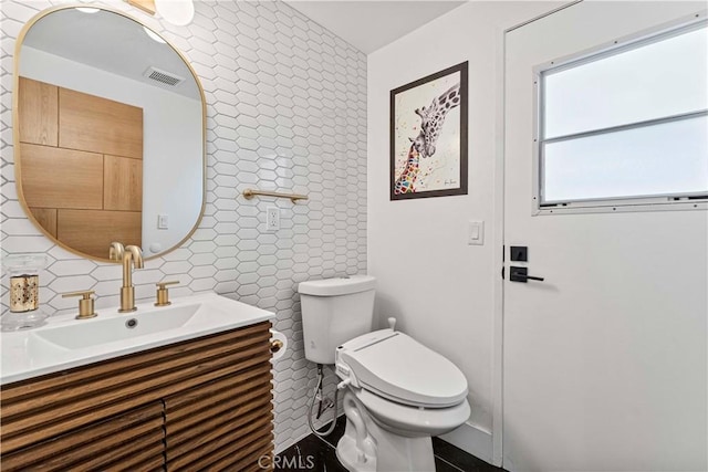 bathroom featuring toilet, vanity, backsplash, and visible vents