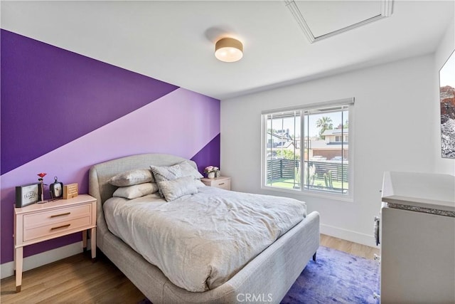 bedroom with wood finished floors, attic access, and baseboards