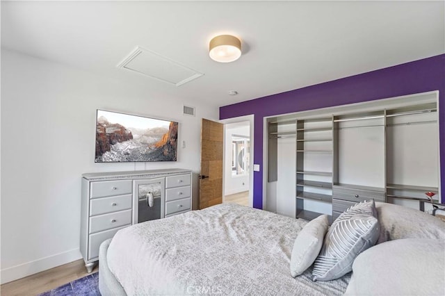 bedroom with a closet, visible vents, wood finished floors, attic access, and baseboards