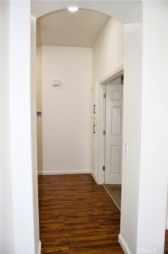 hall with arched walkways, baseboards, and dark wood finished floors