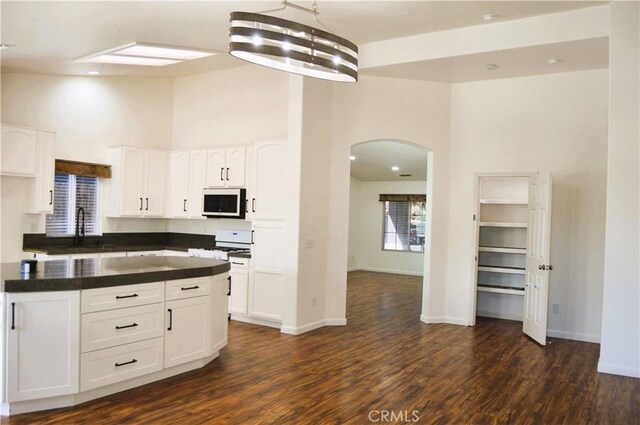 kitchen with arched walkways, a sink, dark countertops, white appliances, and a towering ceiling