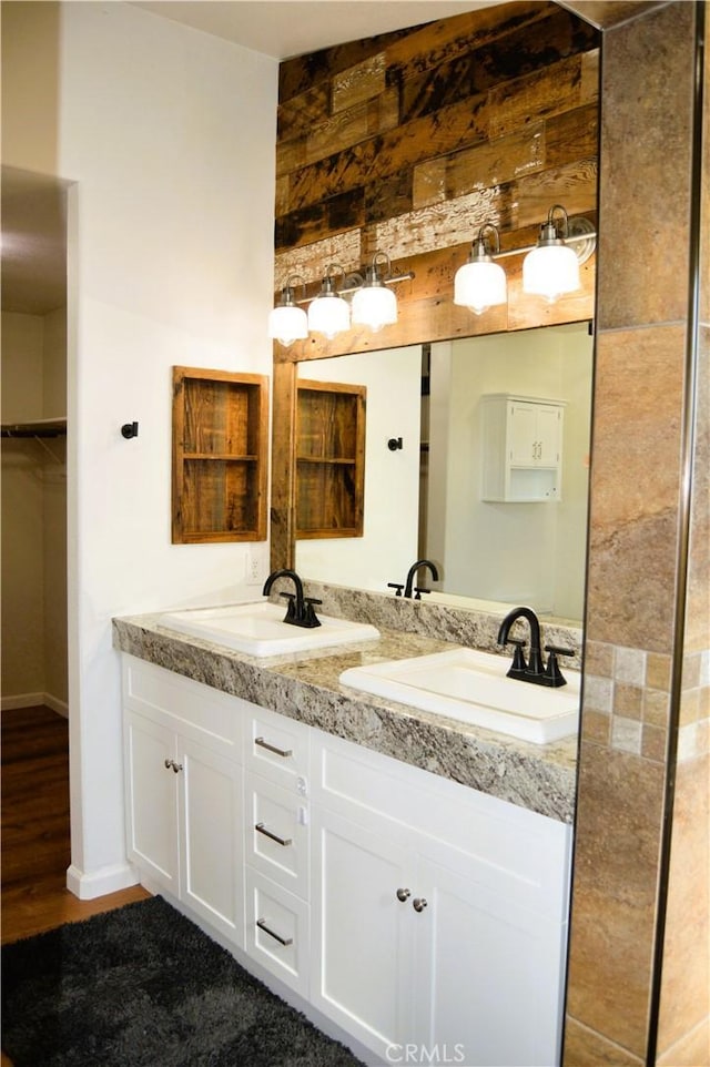 full bathroom featuring baseboards, double vanity, a walk in closet, a sink, and wood finished floors