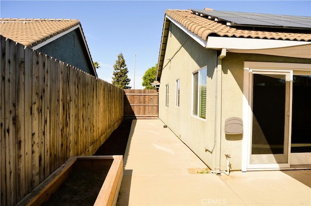 view of home's exterior with a tiled roof, a fenced backyard, stucco siding, a patio, and solar panels