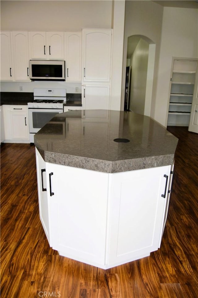 kitchen with a center island, white cabinets, arched walkways, dark countertops, and white range with gas stovetop