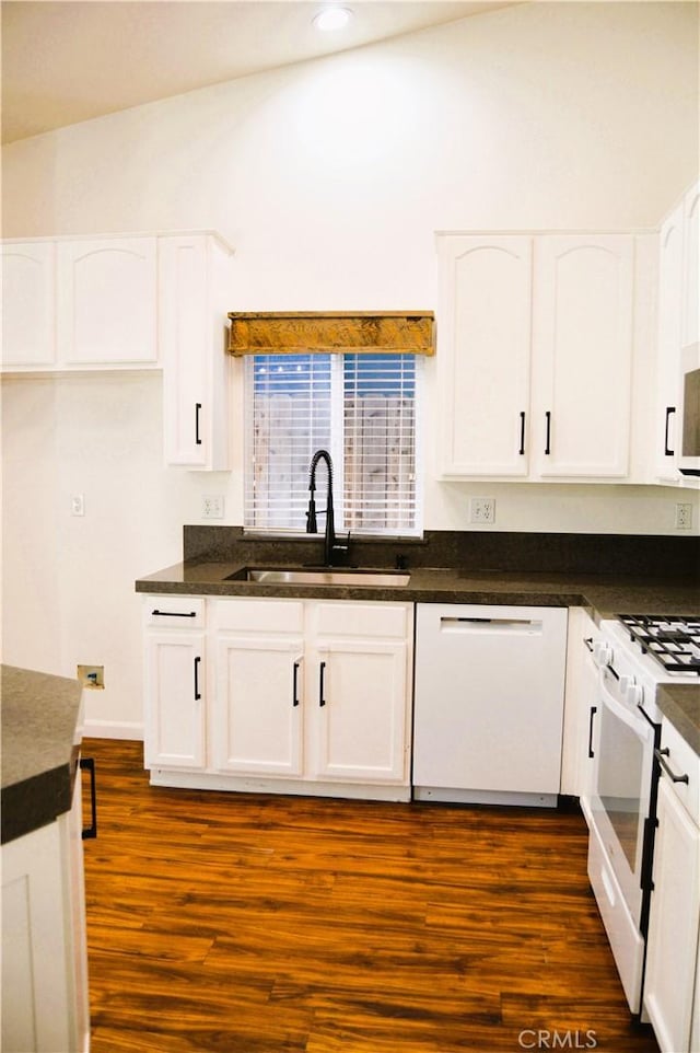 kitchen with a sink, dark countertops, white appliances, and white cabinetry