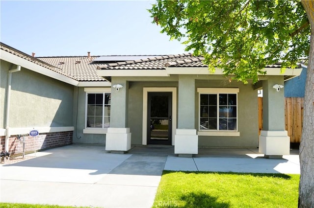 entrance to property with a tiled roof, a patio area, stucco siding, and fence