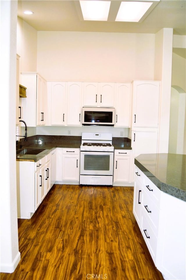 kitchen featuring white cabinetry, a sink, white gas stove, and dark countertops