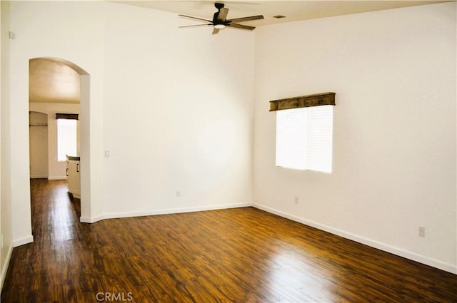 spare room featuring arched walkways, baseboards, a ceiling fan, and dark wood finished floors