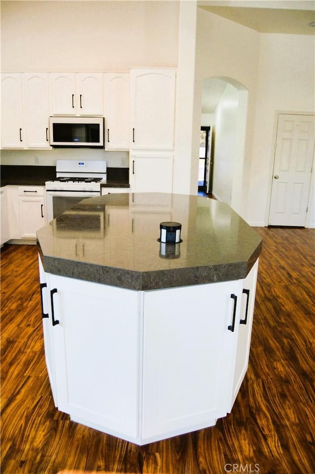 kitchen featuring white appliances, dark wood-style floors, dark countertops, white cabinets, and arched walkways