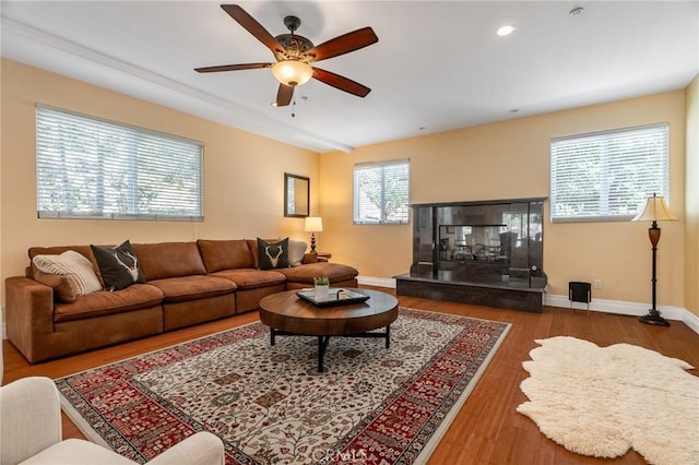 living area with baseboards, a ceiling fan, a glass covered fireplace, and wood finished floors