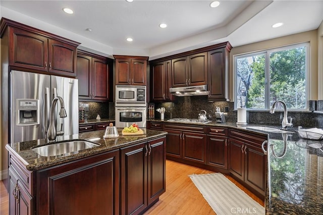 kitchen featuring a sink, stainless steel appliances, dark stone countertops, under cabinet range hood, and a kitchen island