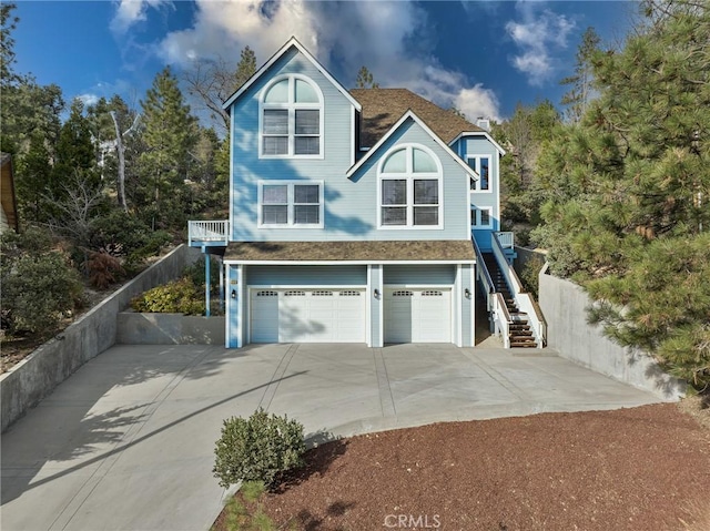 view of front of home with concrete driveway, stairway, a shingled roof, and an attached garage
