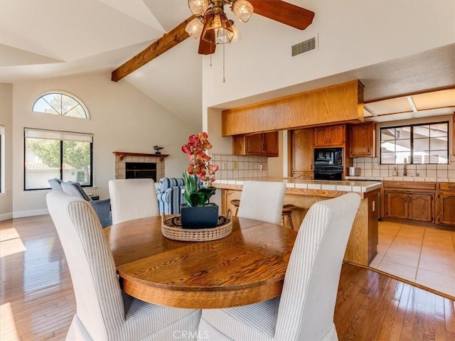 101 Searidge Ct, Pismo Beach, CA 93449 - dining space featuring a ceiling fan, beam ceiling, light wood-style floors, high vaulted ceiling, and a tiled fireplace