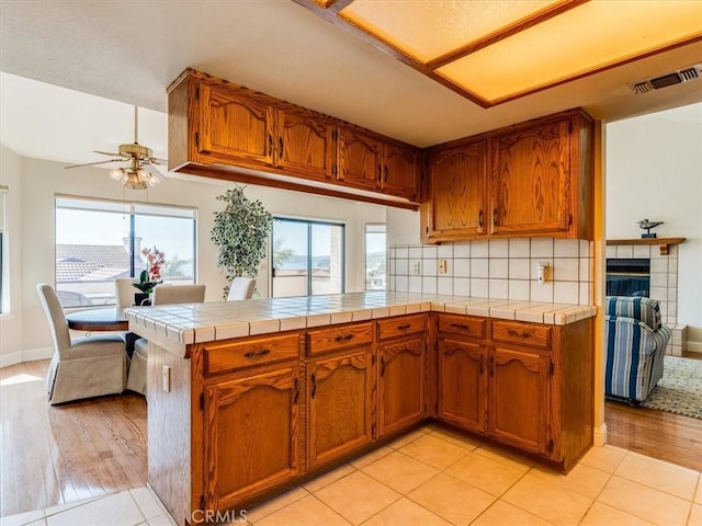 101 Searidge Ct, Pismo Beach, CA 93449 - kitchen featuring a ceiling fan, brown cabinetry, tile countertops, backsplash, and light wood-type flooring