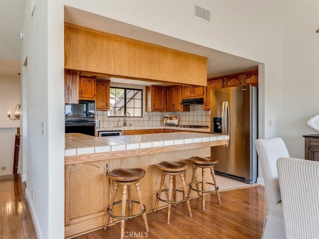 101 Searidge Ct, Pismo Beach, CA 93449 - kitchen with stainless steel fridge with ice dispenser, tile countertops, a peninsula, light wood-style floors, and decorative backsplash