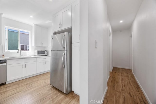 kitchen featuring light wood-style floors, a sink, white cabinetry, and stainless steel appliances