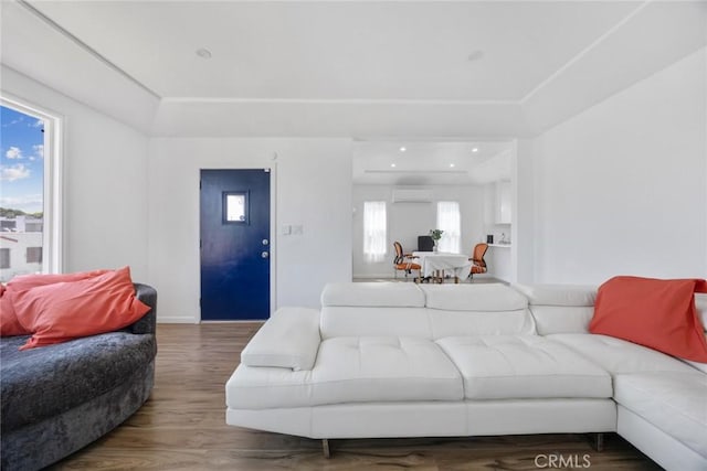 living area with baseboards, a wall unit AC, and wood finished floors