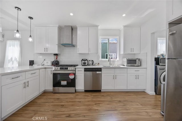 kitchen featuring appliances with stainless steel finishes, tasteful backsplash, a sink, white cabinets, and wall chimney exhaust hood
