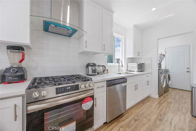 kitchen with washing machine and dryer, light wood-style floors, light countertops, wall chimney exhaust hood, and appliances with stainless steel finishes