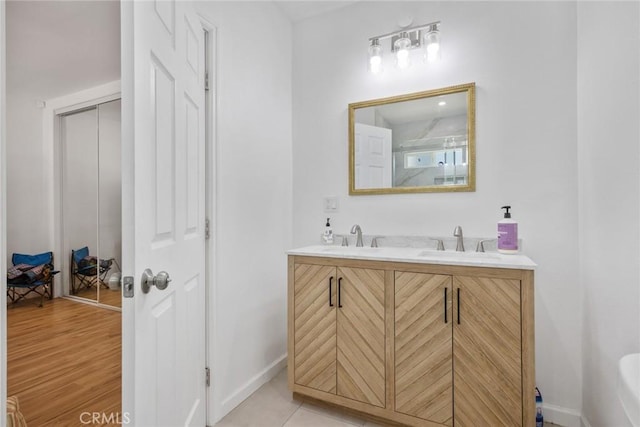 full bathroom with a sink, baseboards, a shower with door, and double vanity