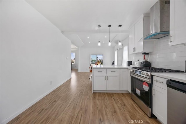 kitchen with a peninsula, wall chimney exhaust hood, white cabinets, light wood-style flooring, and stainless steel appliances