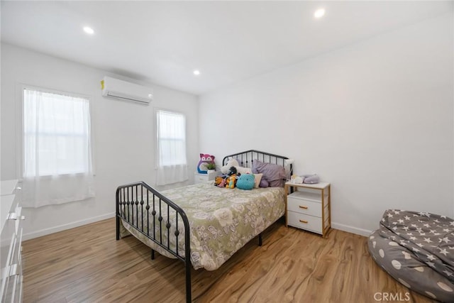 bedroom featuring recessed lighting, baseboards, a wall mounted AC, and light wood-type flooring