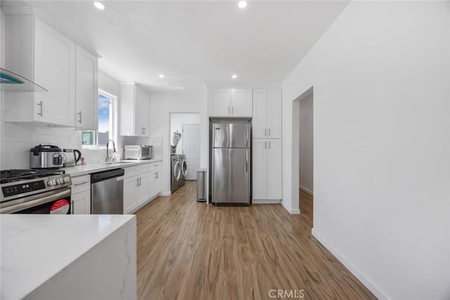 kitchen featuring wall chimney range hood, appliances with stainless steel finishes, white cabinetry, and washer and clothes dryer