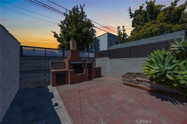 patio terrace at dusk featuring fence and an outdoor brick fireplace