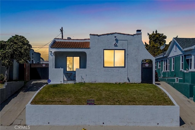 mediterranean / spanish-style home featuring a tiled roof, stucco siding, a yard, and fence