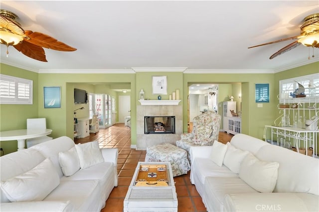 living room featuring ceiling fan, a tiled fireplace, ornamental molding, and plenty of natural light