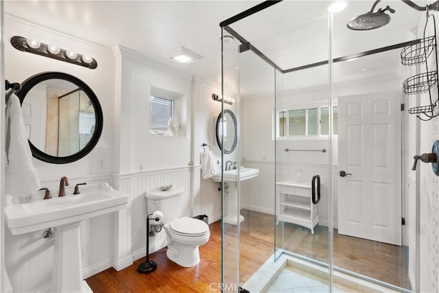 full bathroom with toilet, crown molding, wood finished floors, a wainscoted wall, and a stall shower