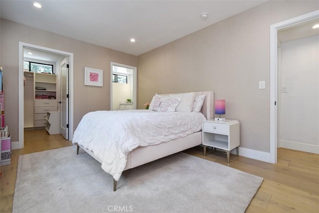 bedroom with a spacious closet, recessed lighting, wood finished floors, and baseboards