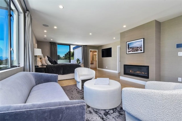 living area with baseboards, recessed lighting, a glass covered fireplace, and wood finished floors
