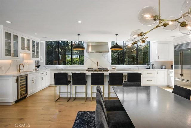 kitchen with glass insert cabinets, light countertops, light wood-style flooring, appliances with stainless steel finishes, and beverage cooler