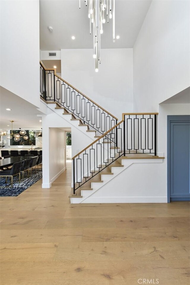 stairs featuring visible vents, baseboards, a towering ceiling, and wood finished floors