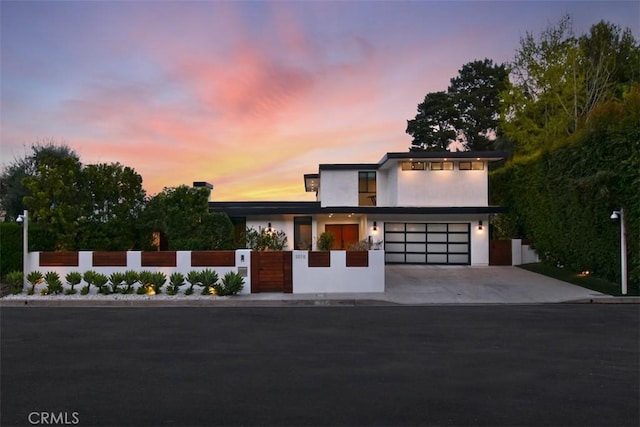 modern home featuring concrete driveway, stucco siding, a garage, and a fenced front yard