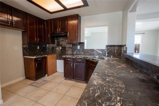 kitchen with light tile patterned floors, tasteful backsplash, under cabinet range hood, a sink, and baseboards