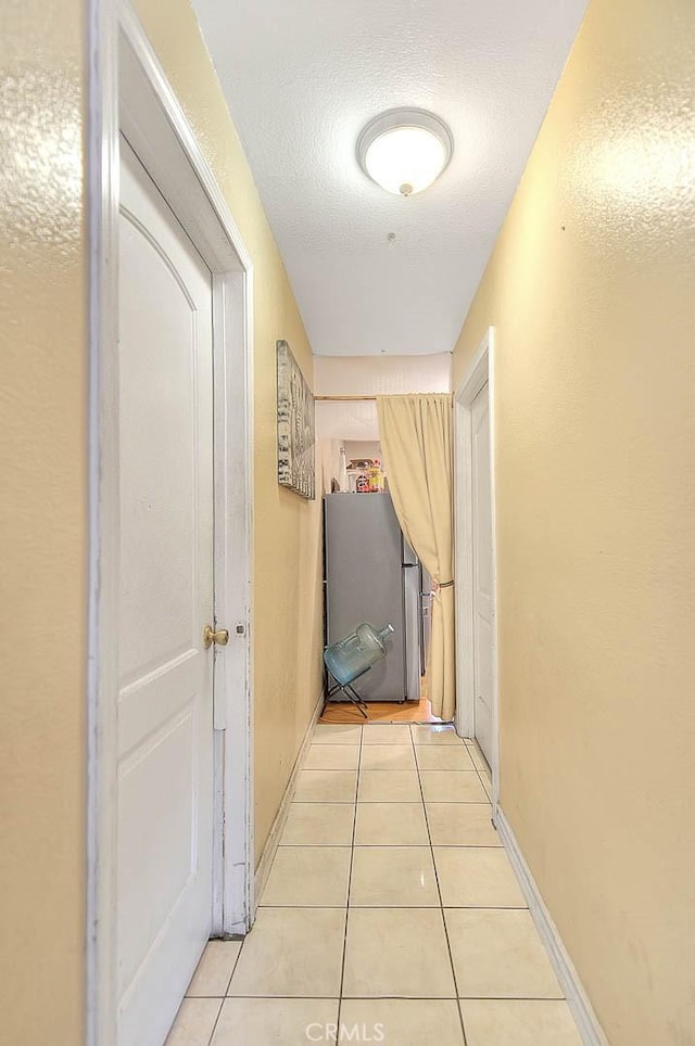 hallway featuring light tile patterned floors, baseboards, and a textured ceiling