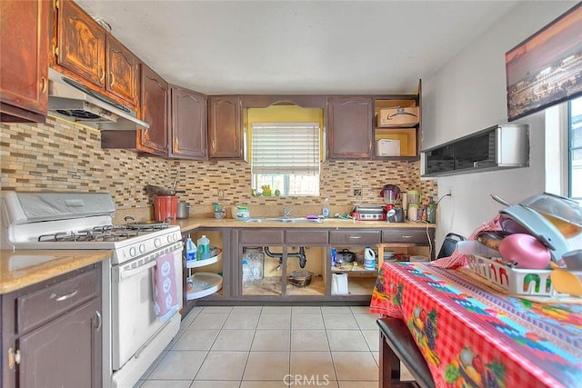 kitchen featuring light tile patterned floors, light countertops, white range with gas stovetop, under cabinet range hood, and a sink