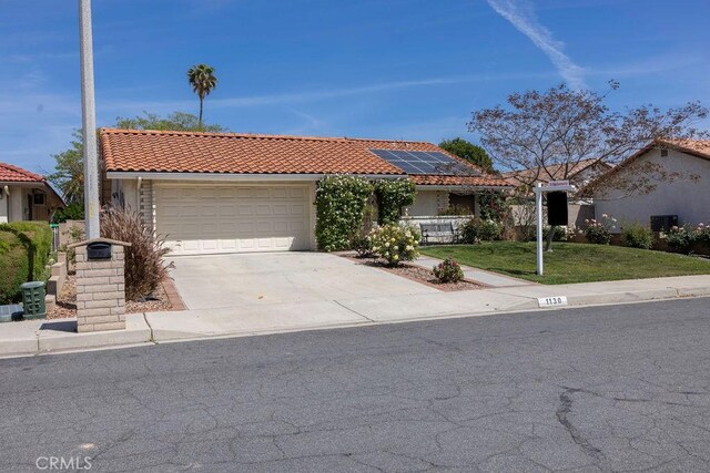 1130 Carob Ct, Hemet, CA 92545 - view of front of house with an attached garage, driveway, a tiled roof, roof mounted solar panels, and a front yard