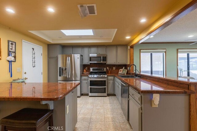 1130 Carob Ct, Hemet, CA 92545 - kitchen with stainless steel appliances, gray cabinets, a peninsula, a tray ceiling, and recessed lighting