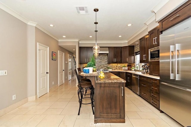 kitchen featuring a breakfast bar area, decorative backsplash, crown molding, built in appliances, and visible vents